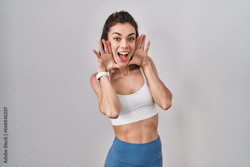 Hispanic woman wearing sportswear over isolated background smiling cheerful playing peek a boo with hands showing face. surprised and exited Hispanic woman wearing sportswear over isolated background smiling cheerful playing peek a boo with hands showing face. surprised and exited
