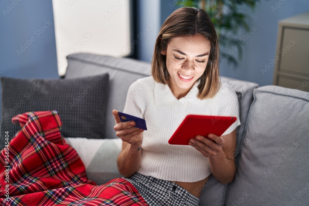 Young beautiful hispanic woman using touchpad and credit card sitting on sofa at home Young beautiful hispanic woman using touchpad and credit card sitting on sofa at home