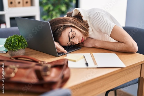 Young beautiful hispanic woman business worker sleeping with head on laptop at office