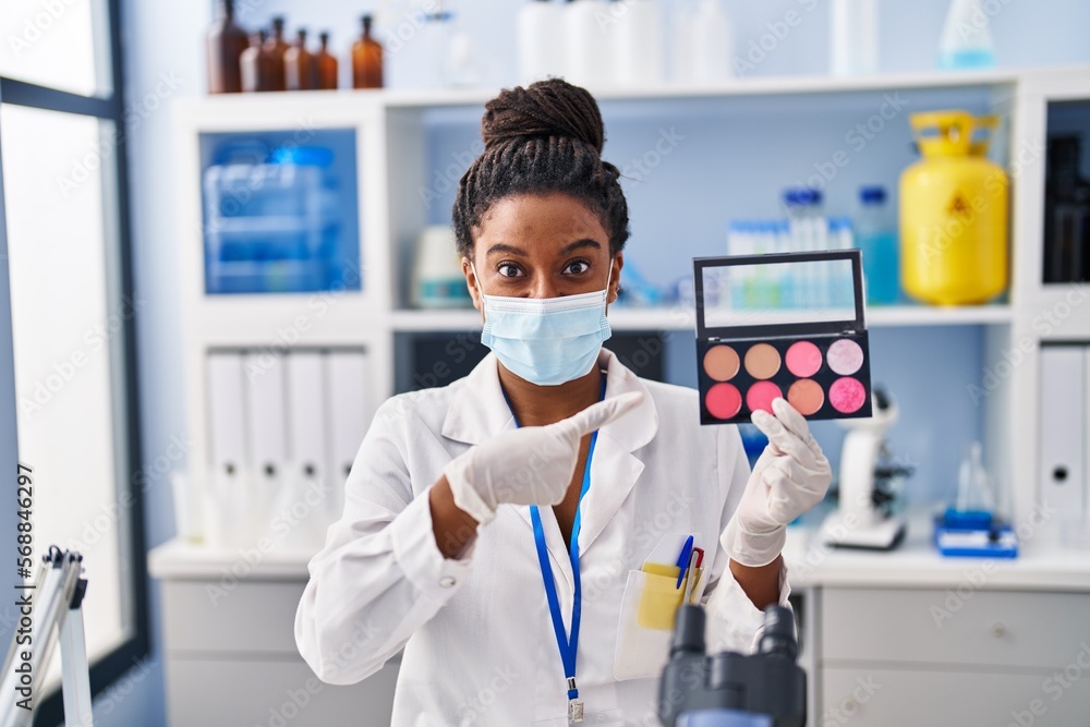 Young african american with braids working at scientist laboratory doing make up smiling happy pointing with hand and finger Young african american with braids working at scientist laboratory doing make up smiling happy pointing with hand and finger