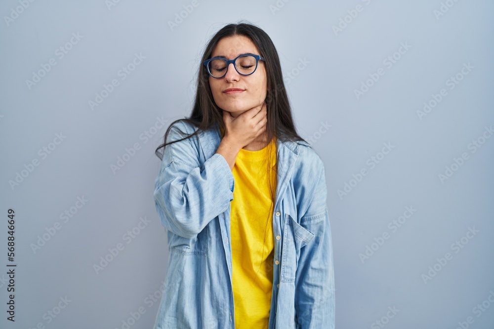 Young hispanic woman standing over blue background touching painful neck, sore throat for flu, clod and infection Young hispanic woman standing over blue background touching painful neck, sore throat for flu, clod and infection