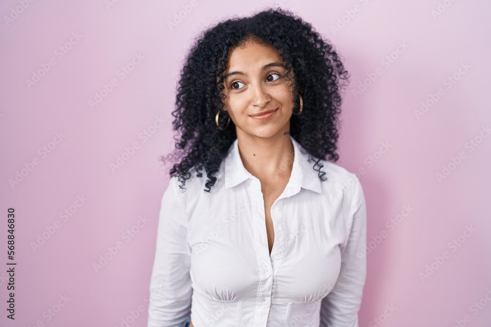 Hispanic woman with curly hair standing over pink background smiling looking to the side and staring away thinking. Hispanic woman with curly hair standing over pink background smiling looking to the side and staring away thinking.