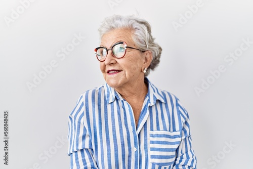 Senior woman with grey hair standing over white background looking away to side with smile on face, natural expression. laughing confident.