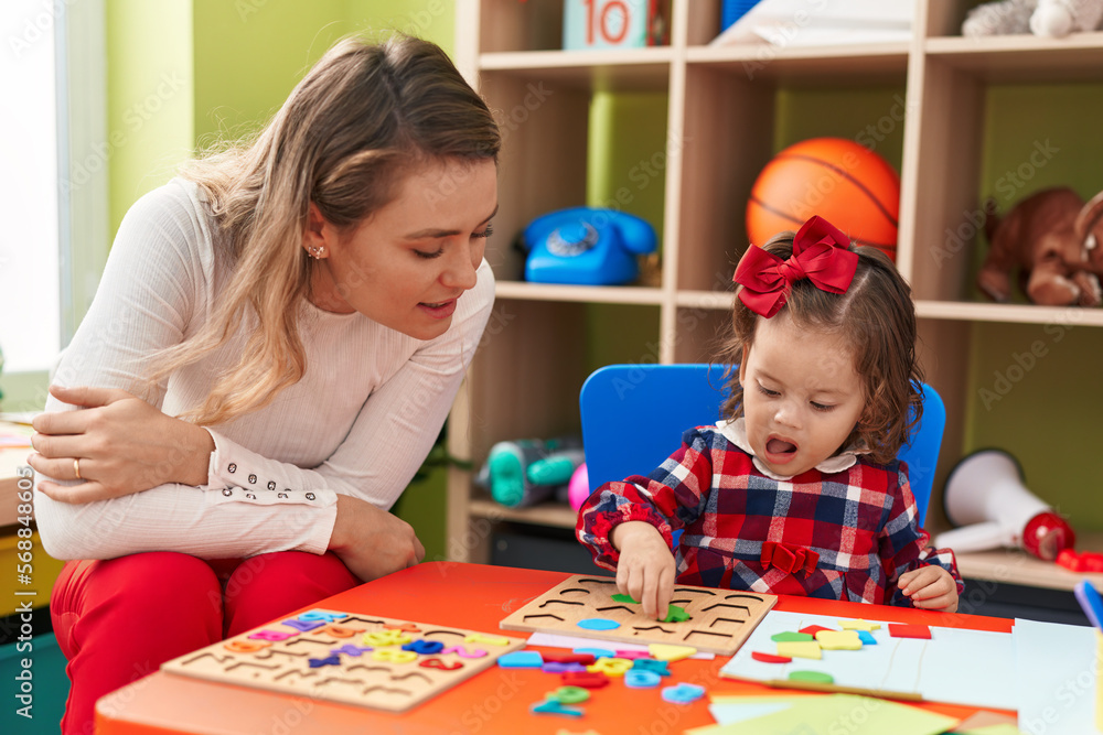 Fototapeta premium Teacher and toddler playing with maths puzzle game sitting on table at kindergarten