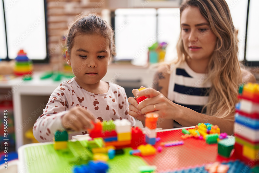 Fototapeta premium Teacher and toddler playing with construction blocks sitting on table at kindergarten
