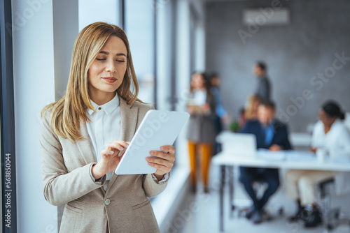 Portrait of happy blond businesswoman using digital tablet in agency. Successful business woman in casual clothing working on tablet. Mixed race young woman looking at camera in creative office. photo