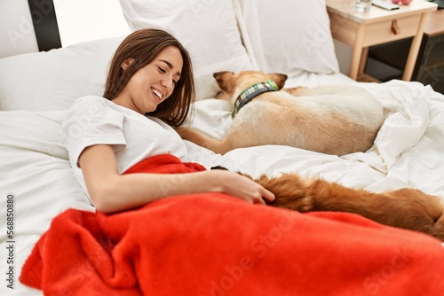 Young hispanic woman hugging dog lying on bed at bedroom