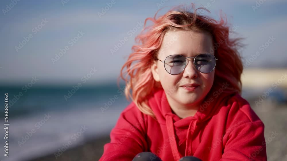 a stylish teenage girl is sitting on the beach on a sunny day in protective glasses she has dyed red hair a stylish teenage girl is sitting on the beach on a sunny day in protective glasses she has dyed red hair