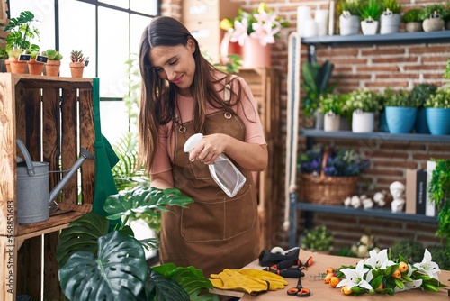 Young beautiful hispanic woman florist using difusser working at flower shop photo