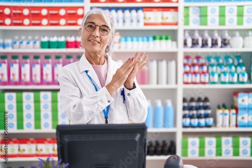 Middle age woman with tattoos working at pharmacy drugstore clapping and applauding happy and joyful, smiling proud hands together