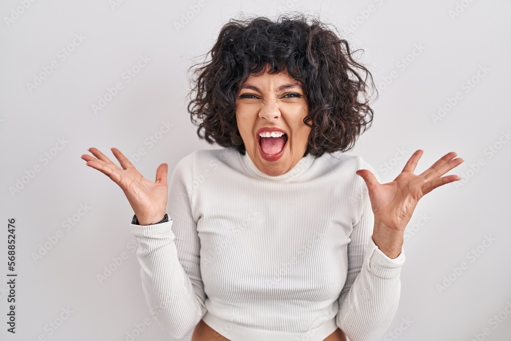 Hispanic woman with curly hair standing over isolated background celebrating mad and crazy for success with arms raised and closed eyes screaming excited. winner concept Hispanic woman with curly hair standing over isolated background celebrating mad and crazy for success with arms raised and closed eyes screaming excited. winner concept