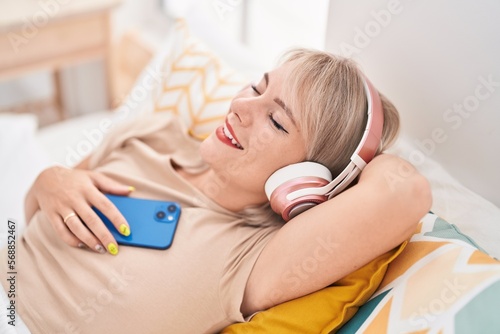 Young blonde woman listening to music relaxed on bed at bedroom