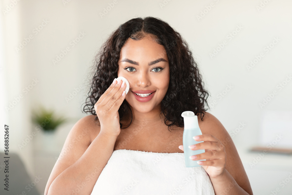 Beautiful black body positive lady cleaning her face from makeup with cotton pads and micellar water, home interior Beautiful black body positive lady cleaning her face from makeup with cotton pads and micellar water, home interior