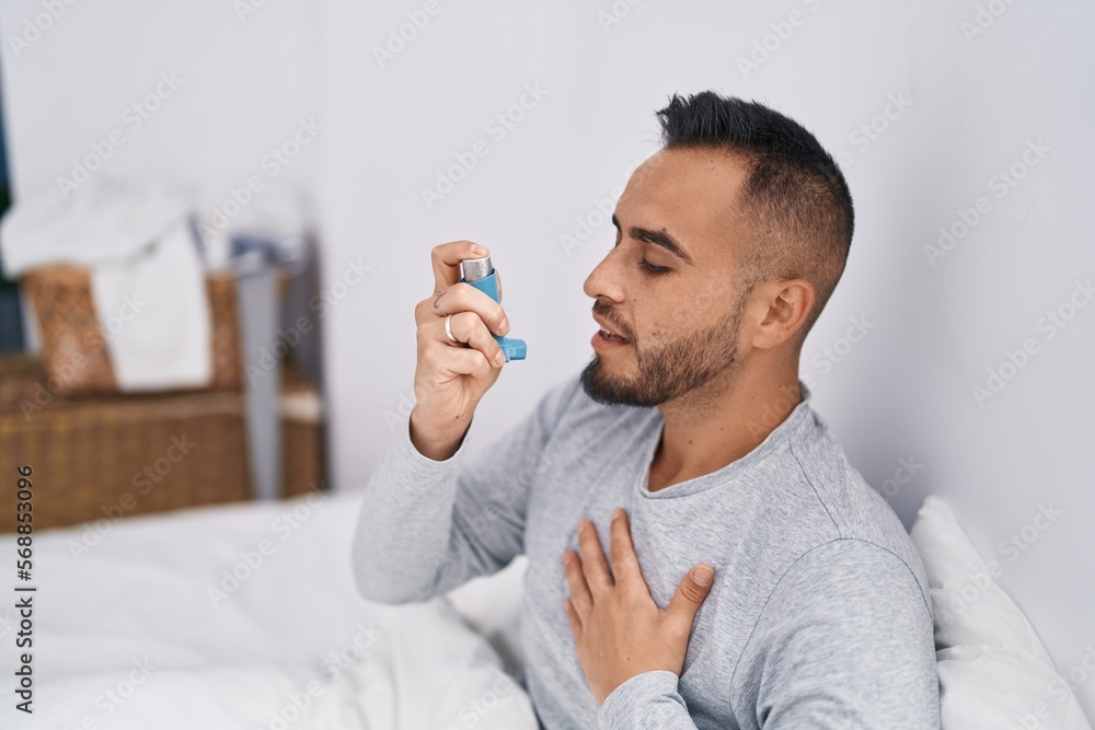 Young hispanic man using inhaler sitting on bed at bedroom Young hispanic man using inhaler sitting on bed at bedroom