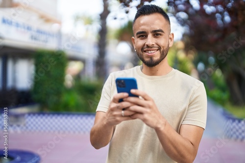 Young hispanic man smiling confident using smartphone at park
