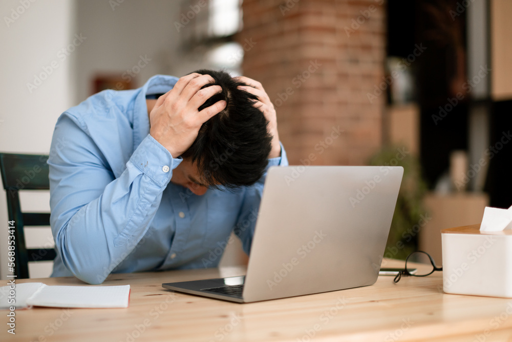 Work problems. Male entrepreneur siting at desk and touching head in despair while working on laptop at home office Work problems. Male entrepreneur siting at desk and touching head in despair while working on laptop at home office