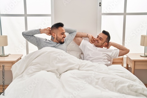 Two men couple waking up stretching arms at bedroom