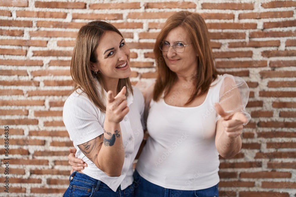 Hispanic mother and daughter wearing casual white t shirt pointing fingers to camera with happy and funny face. good energy and vibes.