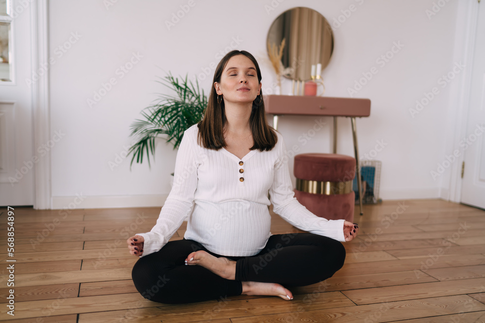 Young pregnant woman sitting in lotus pose with eyes closed Young pregnant woman sitting in lotus pose with eyes closed