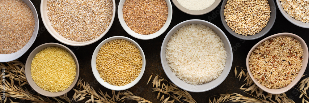 Various grain cereals in bowls banner, top view on a brown background with bowls of cereals and ears of oats