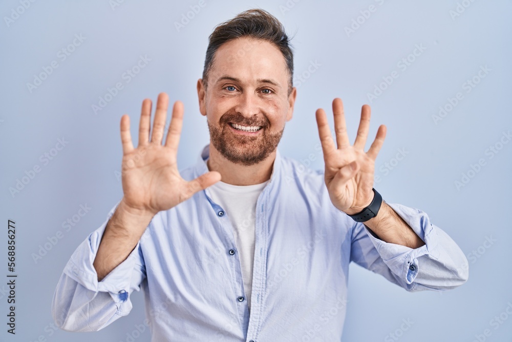 Middle age caucasian man standing over blue background showing and pointing up with fingers number nine while smiling confident and happy. Middle age caucasian man standing over blue background showing and pointing up with fingers number nine while smiling confident and happy.