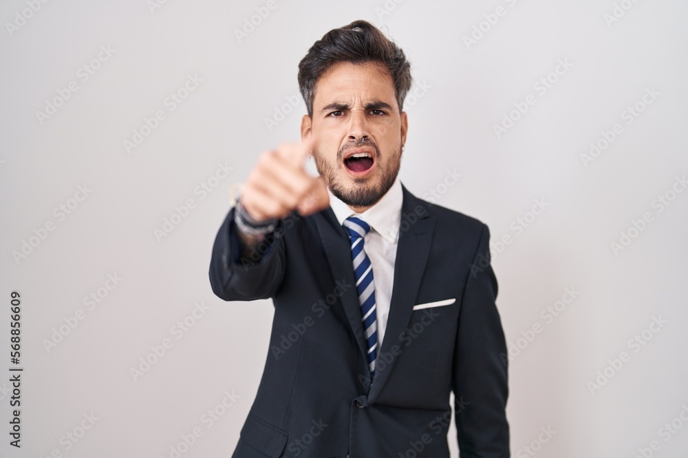Young hispanic man with tattoos wearing business suit and tie pointing displeased and frustrated to the camera, angry and furious with you Young hispanic man with tattoos wearing business suit and tie pointing displeased and frustrated to the camera, angry and furious with you