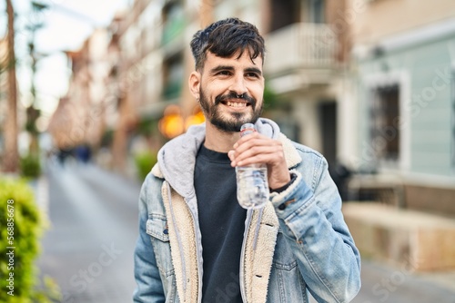 Young hispanic man smiling confident drinking water at street