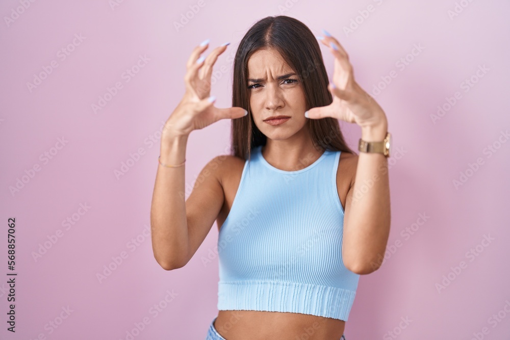 Young brunette woman standing over pink background shouting frustrated with rage, hands trying to strangle, yelling mad Young brunette woman standing over pink background shouting frustrated with rage, hands trying to strangle, yelling mad