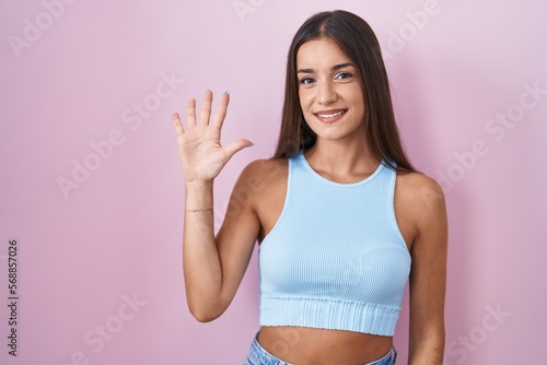 Young brunette woman standing over pink background showing and pointing up with fingers number five while smiling confident and happy.