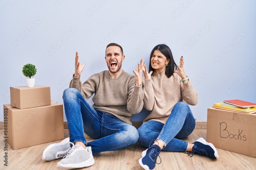 Young couple moving to a new home crazy and mad shouting and yelling with aggressive expression and arms raised. frustration concept. Young couple moving to a new home crazy and mad shouting and yelling with aggressive expression and arms raised. frustration concept.