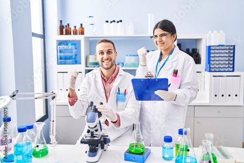 Two young people working at scientist laboratory screaming proud  celebrating victory and success very excited with raised arms