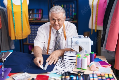 Middle age grey-haired man tailor smiling confident make mark on cloth at tailor shop