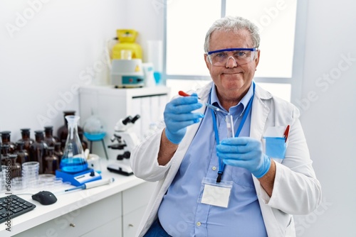 Middle age grey-haired man wearing scientist uniform using pipette at laboratory