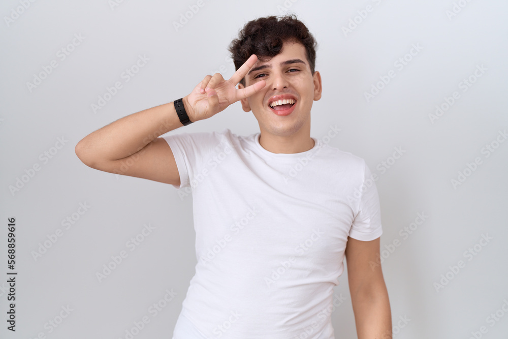 Young non binary man wearing casual white t shirt doing peace symbol with fingers over face, smiling cheerful showing victory Young non binary man wearing casual white t shirt doing peace symbol with fingers over face, smiling cheerful showing victory
