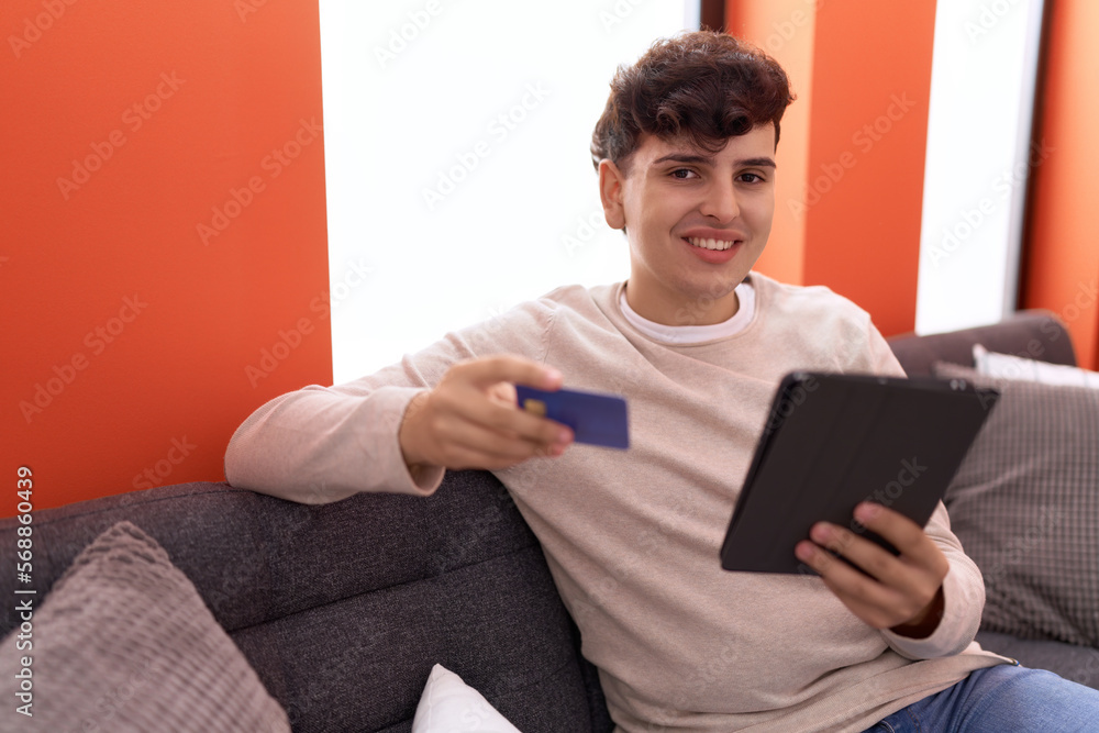 Non binary man using touchpad and credit card sitting on sofa at home Non binary man using touchpad and credit card sitting on sofa at home