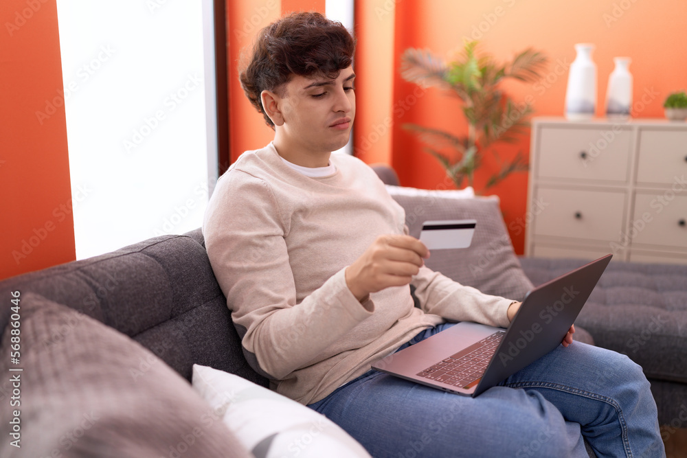 Non binary man using laptop and credit card with worried expression at home Non binary man using laptop and credit card with worried expression at home