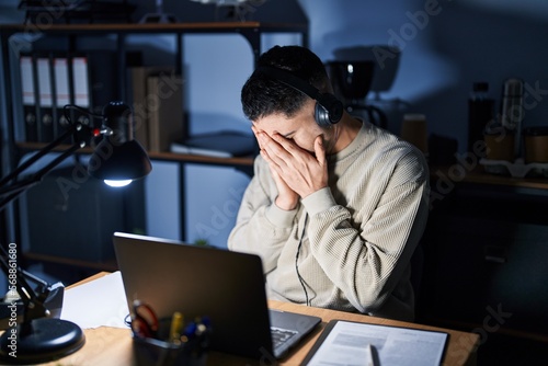 Young handsome man working using computer laptop at night with sad expression covering face with hands while crying. depression concept.