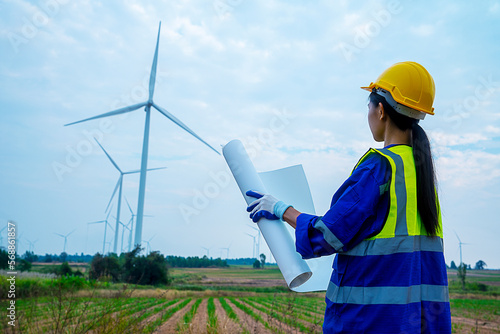 Female engineer mechanic worker in safety uniform and helmet holding blueprint looking at turbine maintenance plan .The concept of renewable natural energy generates electricity.