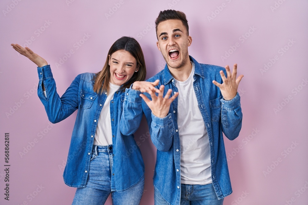 Young hispanic couple standing over pink background celebrating mad and crazy for success with arms raised and closed eyes screaming excited. winner concept Young hispanic couple standing over pink background celebrating mad and crazy for success with arms raised and closed eyes screaming excited. winner concept