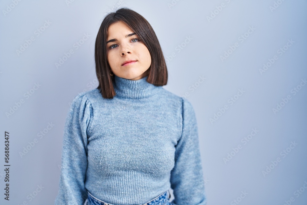 Young hispanic woman standing over blue background relaxed with serious expression on face. simple and natural looking at the camera.