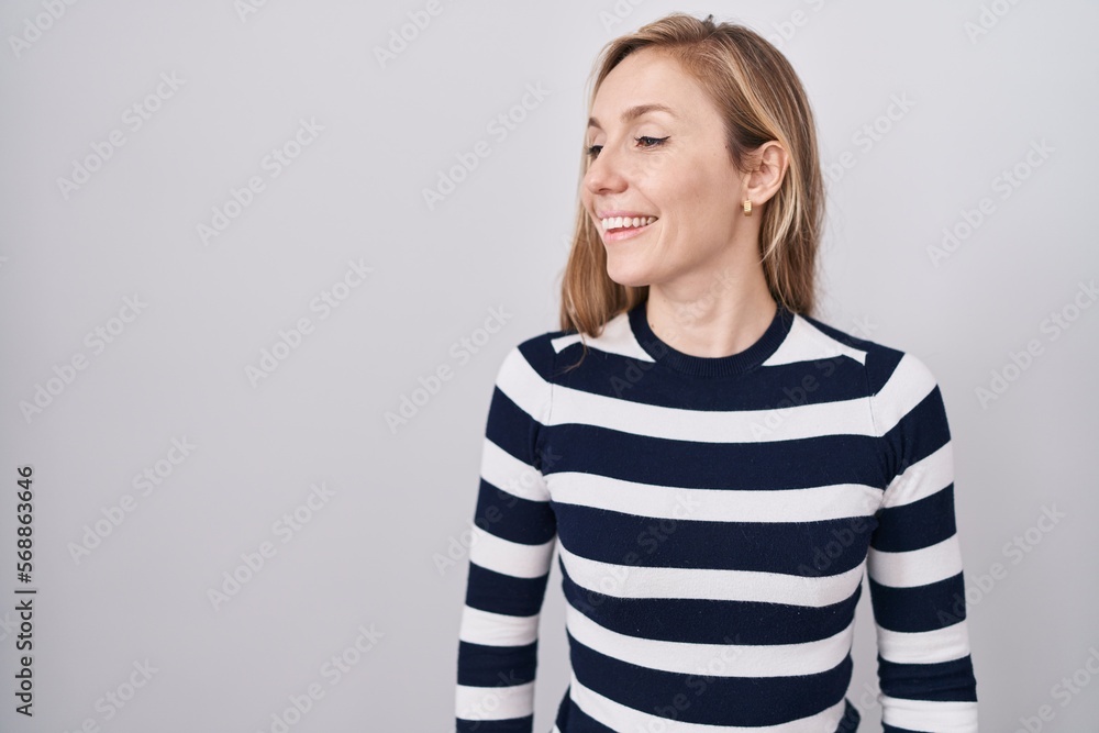 Young caucasian woman wearing casual navy sweater looking away to side with smile on face, natural expression. laughing confident. Young caucasian woman wearing casual navy sweater looking away to side with smile on face, natural expression. laughing confident.