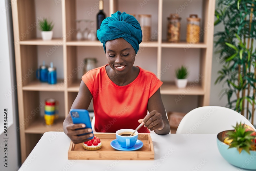 Young african american woman using smartphone having breakfast at home