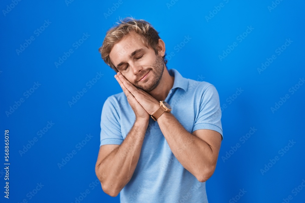 Caucasian man standing over blue background sleeping tired dreaming and posing with hands together while smiling with closed eyes. Caucasian man standing over blue background sleeping tired dreaming and posing with hands together while smiling with closed eyes.