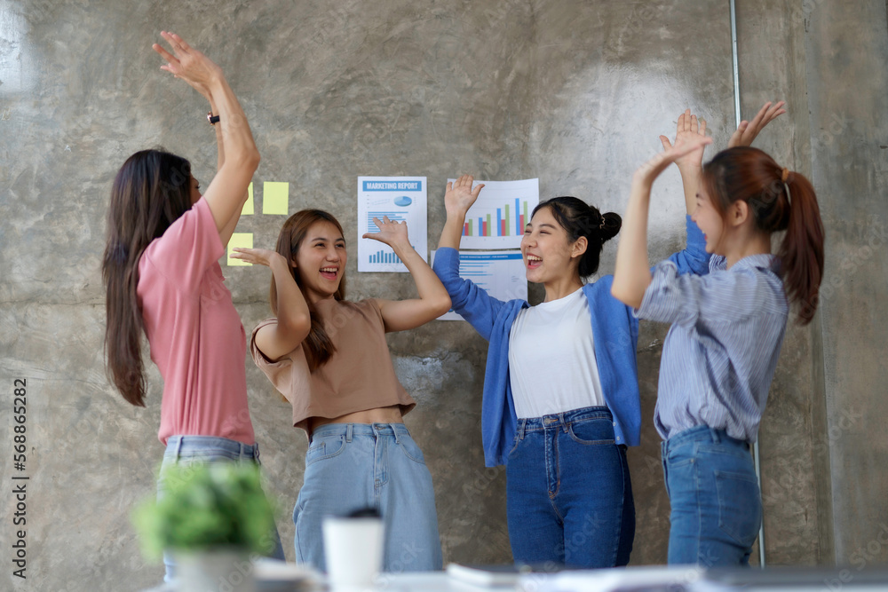 Obraz premium Group of happy asian businesswomen in successful casual clothes raising their fists in joy with success of work done in office smiling.