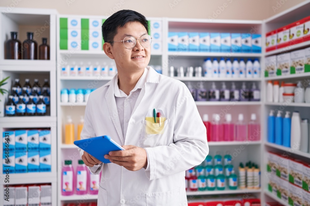 Young chinese man pharmacist using touchpad working at pharmacy Young chinese man pharmacist using touchpad working at pharmacy