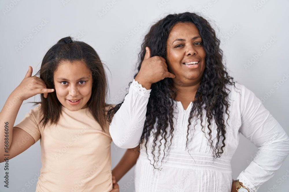Mother and young daughter standing over white background smiling doing phone gesture with hand and fingers like talking on the telephone. communicating concepts. Mother and young daughter standing over white background smiling doing phone gesture with hand and fingers like talking on the telephone. communicating concepts.
