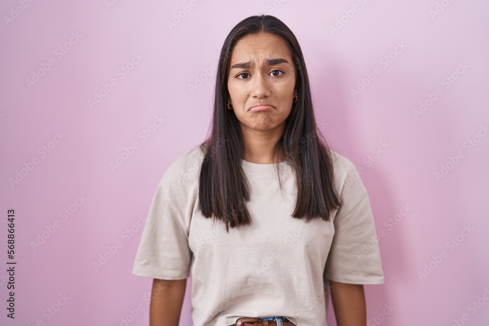 Fototapeta premium Young hispanic woman standing over pink background depressed and worry for distress, crying angry and afraid. sad expression.