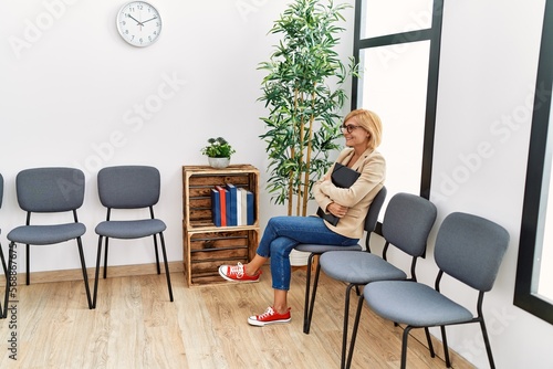 Middle age blonde woman smiling confident holding binder at waiting room