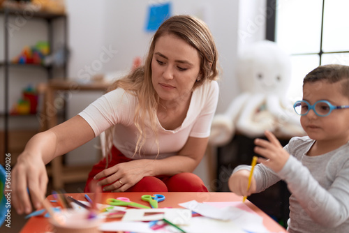 Teacher and toddler sitting on table drawing on paper at kindergarten