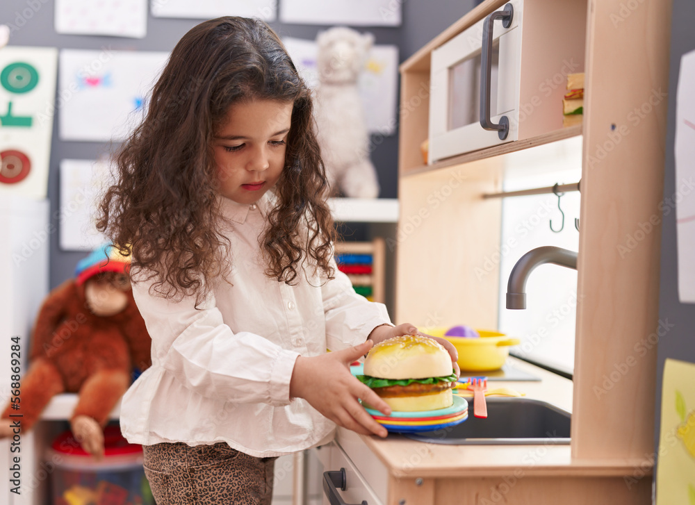 Adorable hispanic girl playing to cook hamburger toy with play kitchen at kindergarten